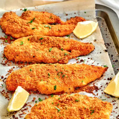 baked panko chicken on a baking sheet with lemon wedges on the side
