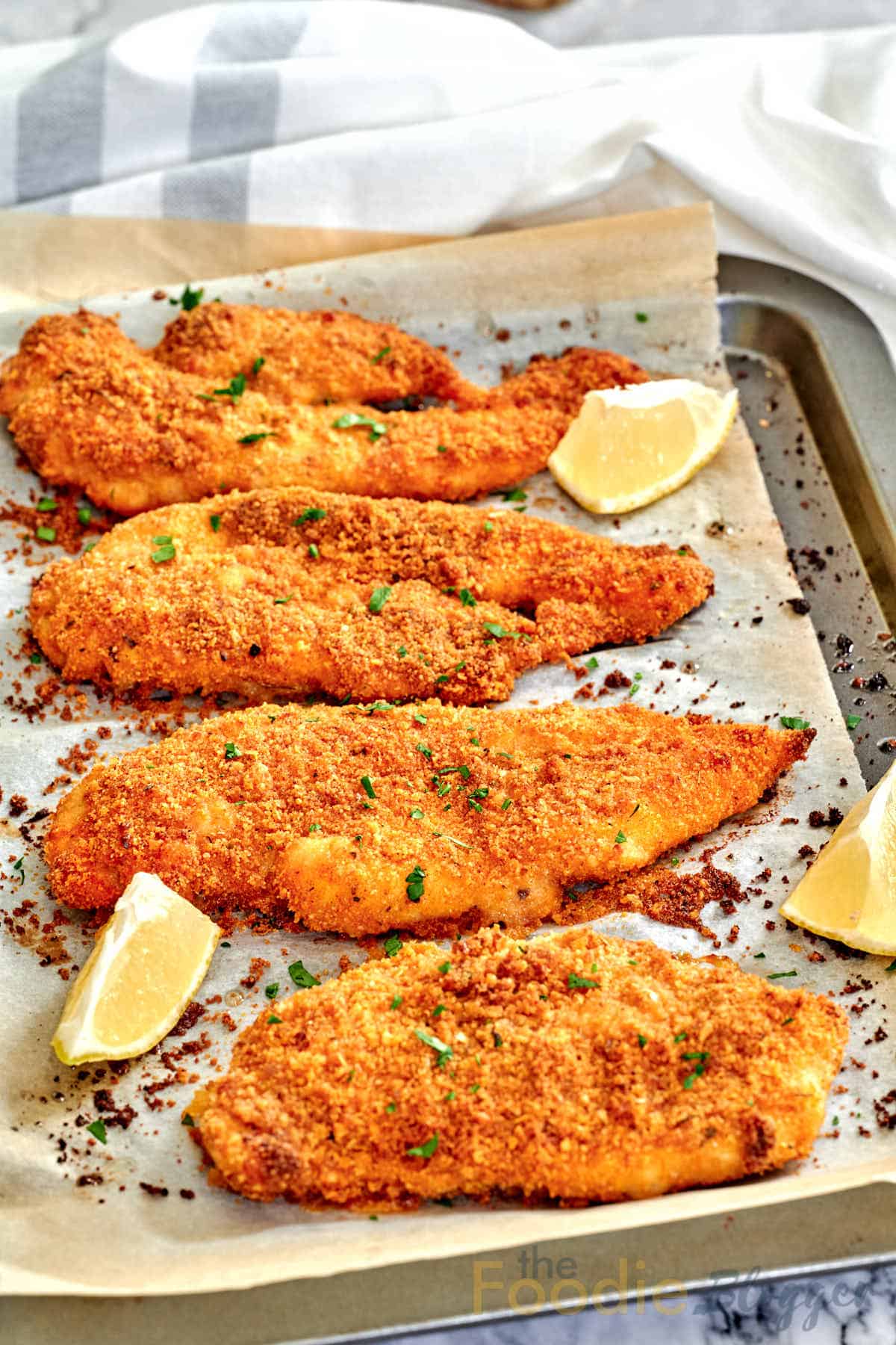 baked panko chicken on a baking sheet with lemon wedges on the side