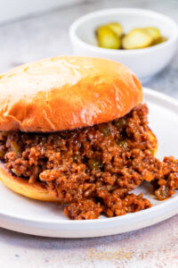 homemade sloppy joes on toasted burger buns with pickles behind