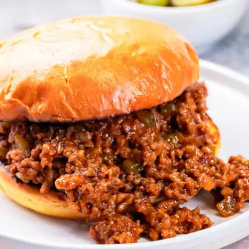 homemade sloppy joes on toasted burger buns with pickles behind