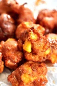 Homemade apple fritters stacked on a plate with a sugar glaze