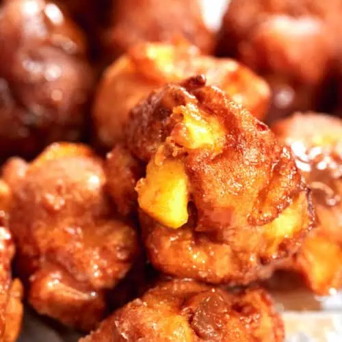 Homemade apple fritters stacked on a plate with a sugar glaze