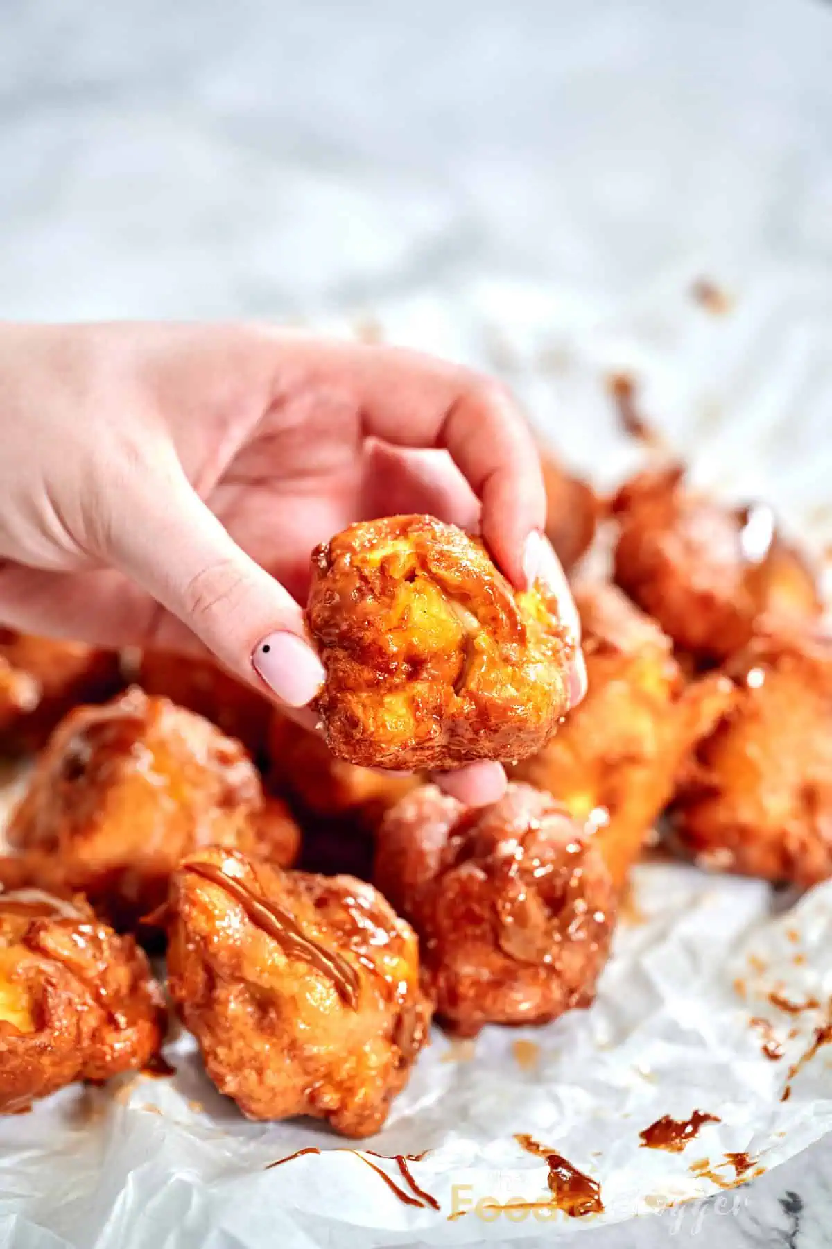 Close-up of a crispy apple fritter held in hand, showing golden-brown exterior.