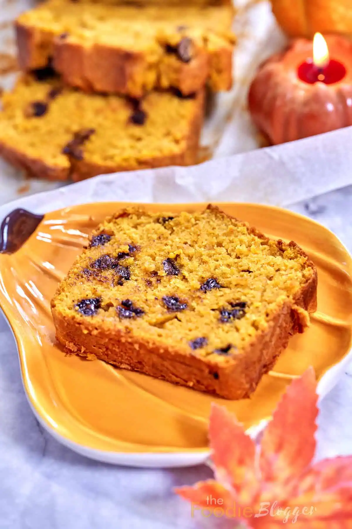 A slice of Pumpkin Chocolate Chip Bread served on a pumpkin shaped plate, highlighting its moist texture and rich chocolate chips.