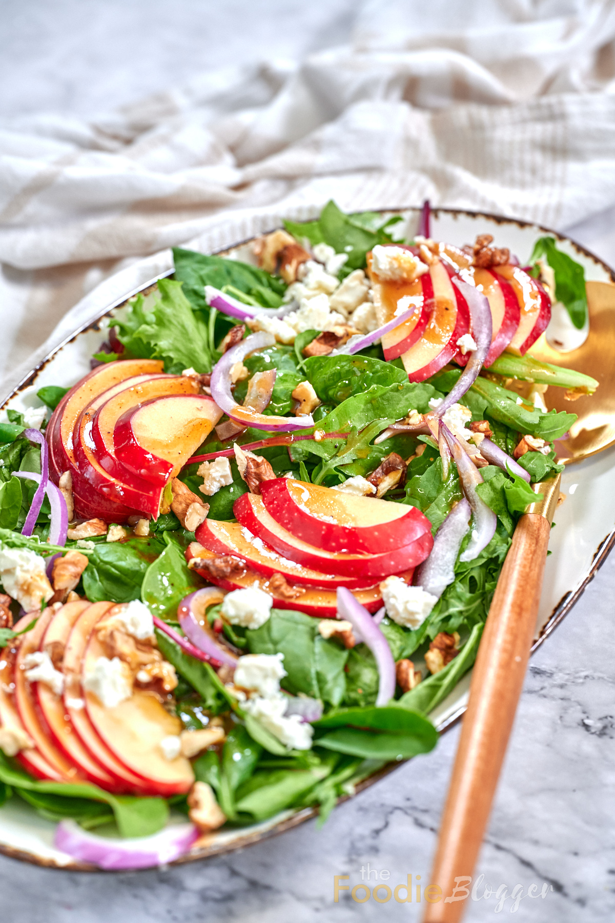 Apple Walnut Salad 2 Mixed-greens salad layered with thin red-apple slices, toasted walnuts, feta crumbles, and red-onion ribbons on an oval platter.