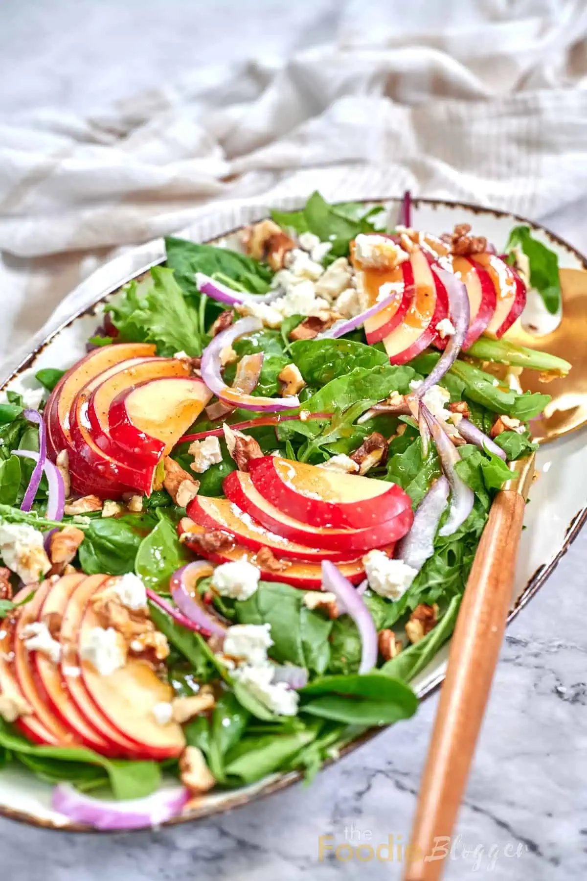 Apple Walnut Salad 2 Mixed-greens salad layered with thin red-apple slices, toasted walnuts, feta crumbles, and red-onion ribbons on an oval platter.