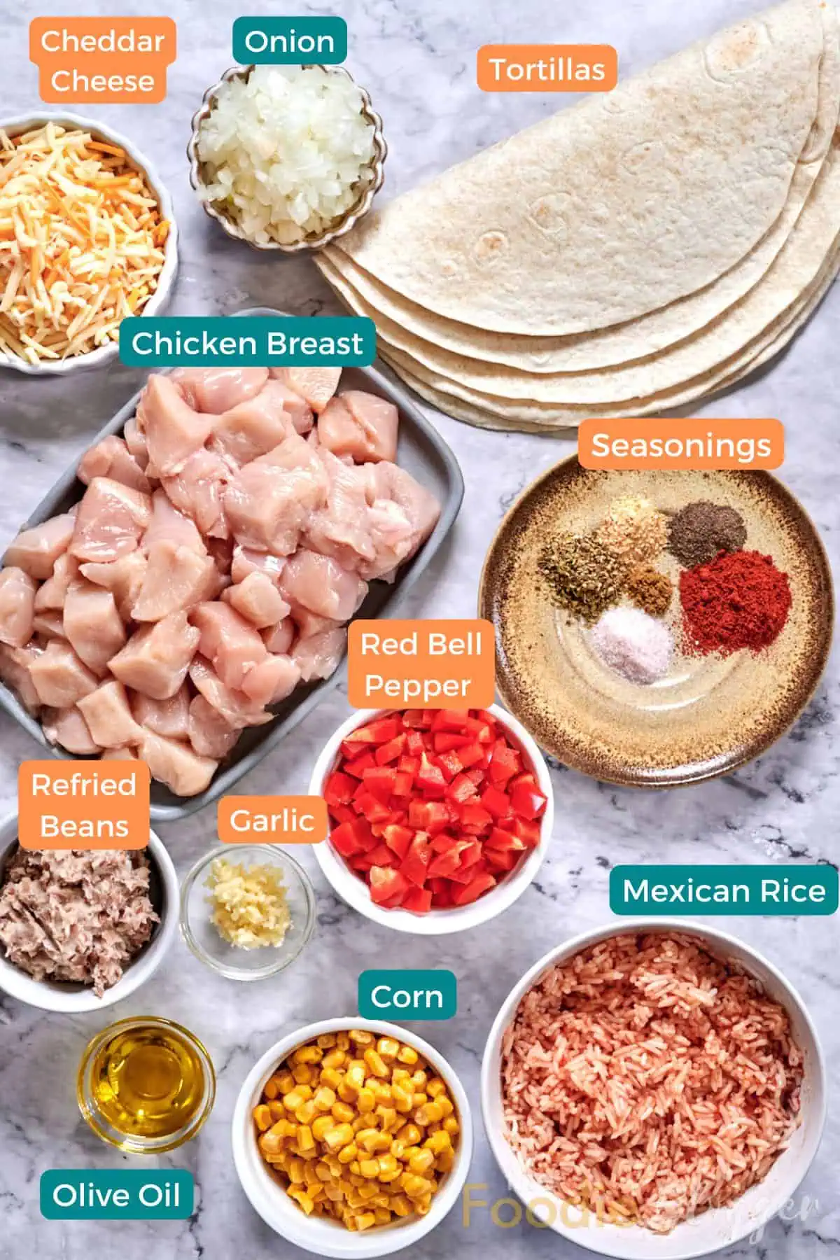 Chicken Burrito 3 Top-down view of labeled ingredients on a marble surface: a platter of cubed chicken, small bowls of shredded cheese, seasonings, chopped veggies, refried beans, and a stack of soft tortillas.