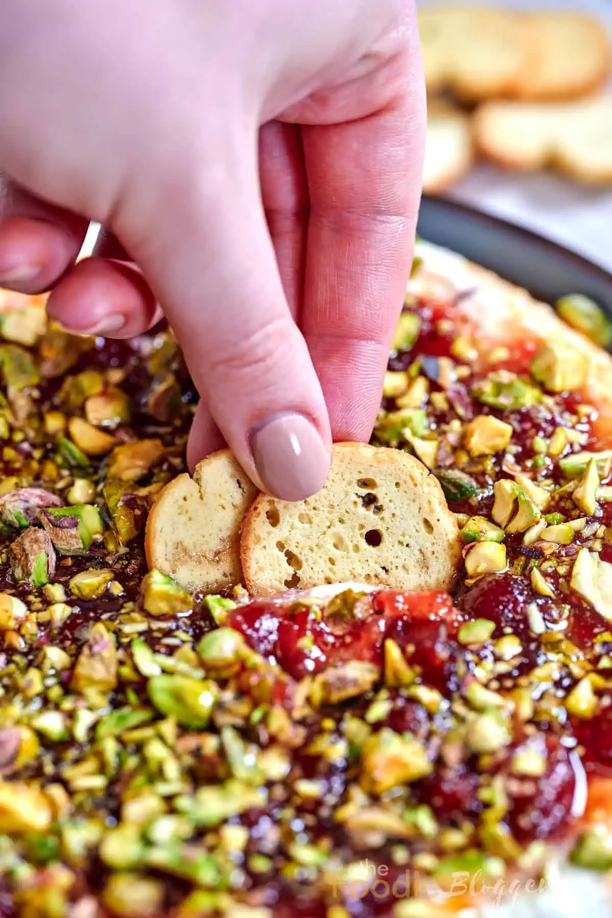 Cranberry Whipped Feta Dip 5 Hand dipping a crispy cracker into creamy cranberry whipped feta dip with crushed pistachios.