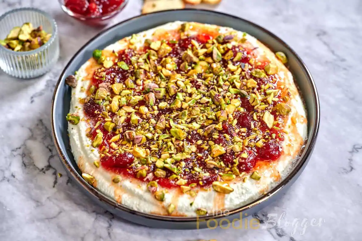 Cranberry Whipped Feta Dip 4 Fresh cranberry whipped feta dip sprinkled with green pistachios, served on a round plate.