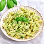 Lunch-ready pesto pasta, pine nuts glistening like little pearls, basil leaves just out of focus in the corner.