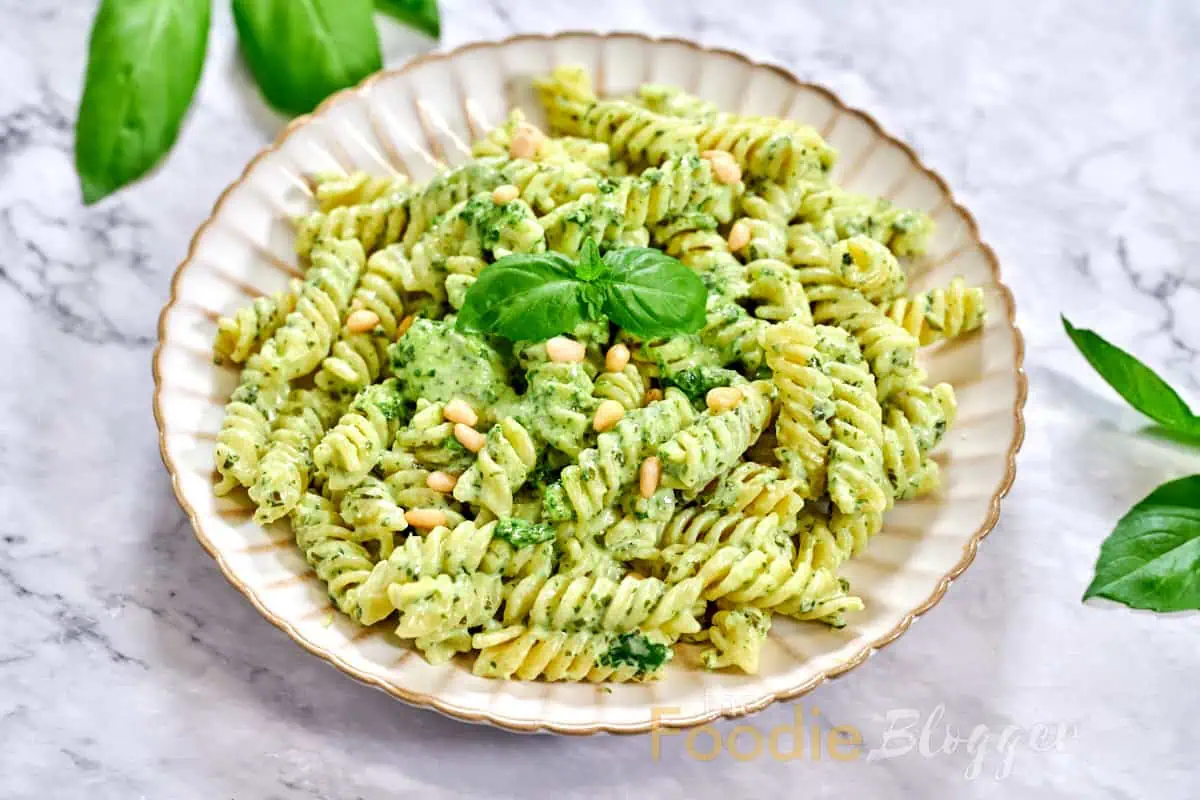 Creamy Pesto Pasta 4 Rich, sauce-coated pasta spirals nestled together, pine nuts and whole basil sprig adding texture and color.