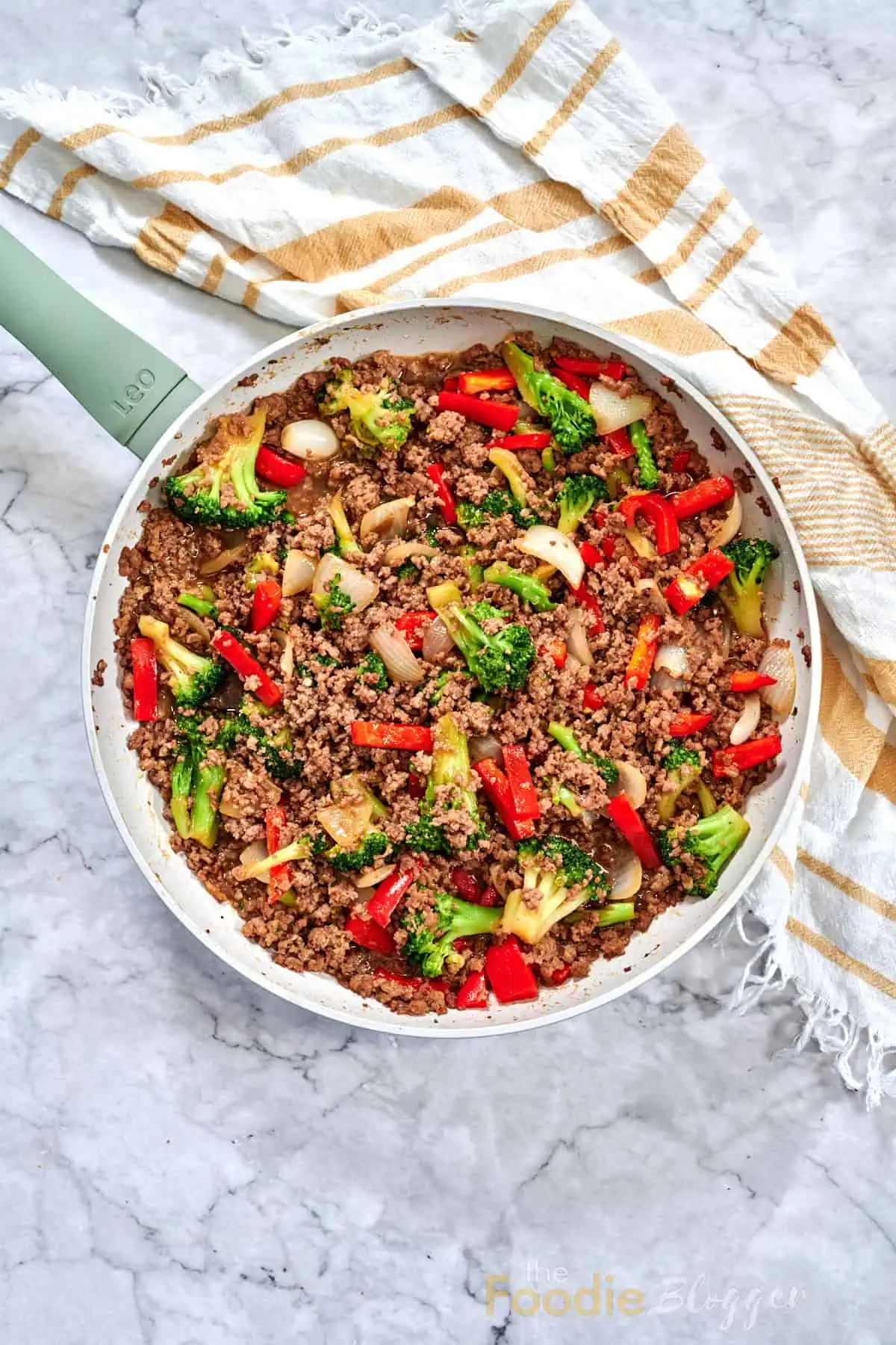 Ground Beef And Broccoli Stir Fry 2 Whole skillet of ground-beef and broccoli stir-fry resting on marble with striped kitchen towel.