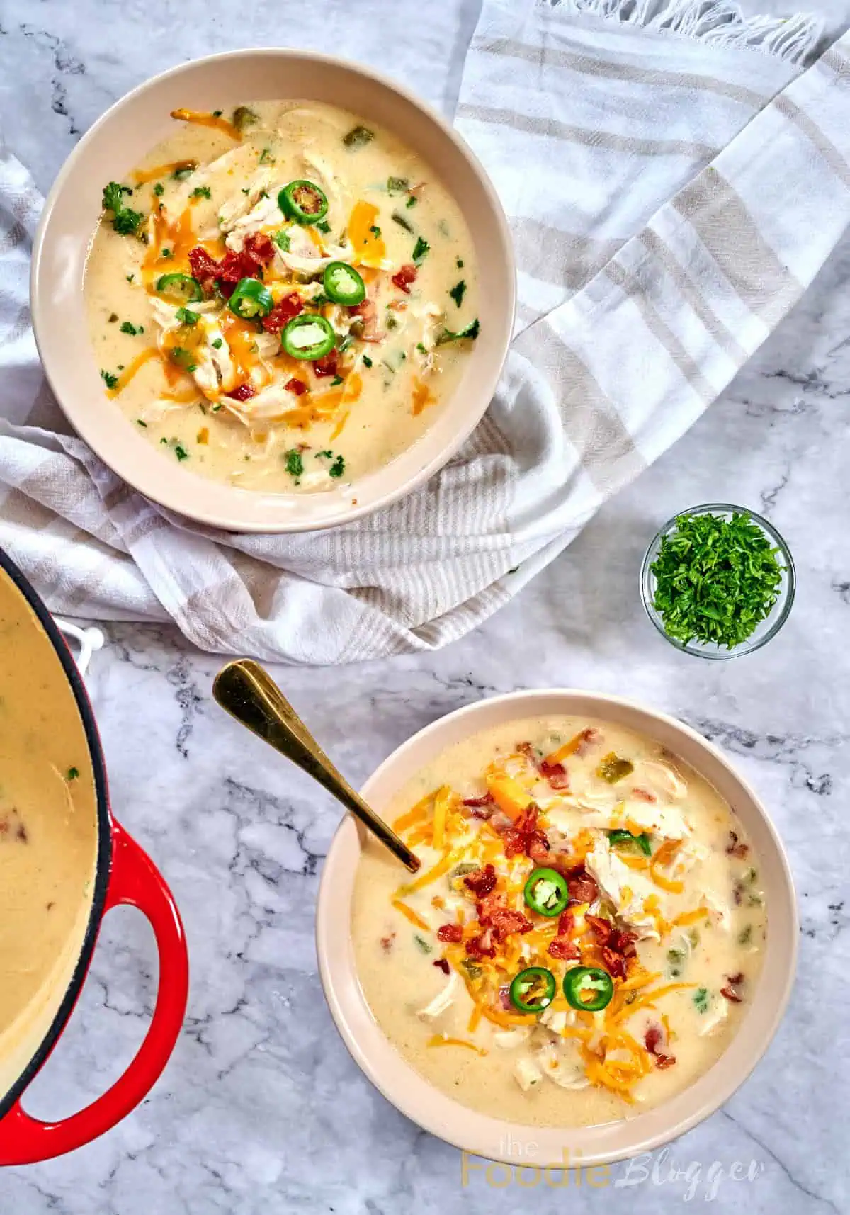 Jalapeno Popper Chicken Soup 2 Creamy jalapeño-popper chicken soup in two bowls, garnished with cheddar, bacon bits, sliced jalapeños, and parsley.