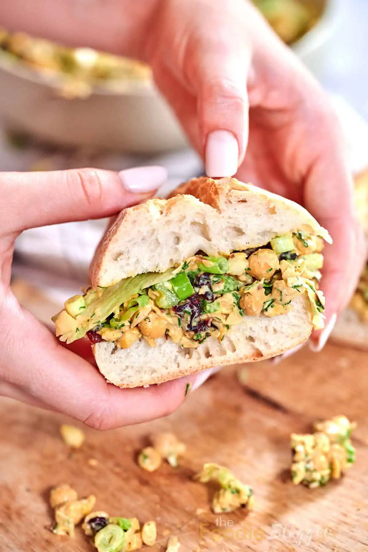 Vegan Chicken Salad 2 Freshly made vegan chicken-salad sandwich held between manicured fingers over a wooden board.