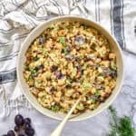 Overhead view of a large bowl of chickpea salad dotted with grapes, celery, and green onions, spoon ready for serving.