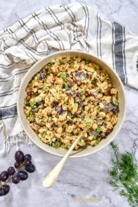 Overhead view of a large bowl of chickpea salad dotted with grapes, celery, and green onions, spoon ready for serving.
