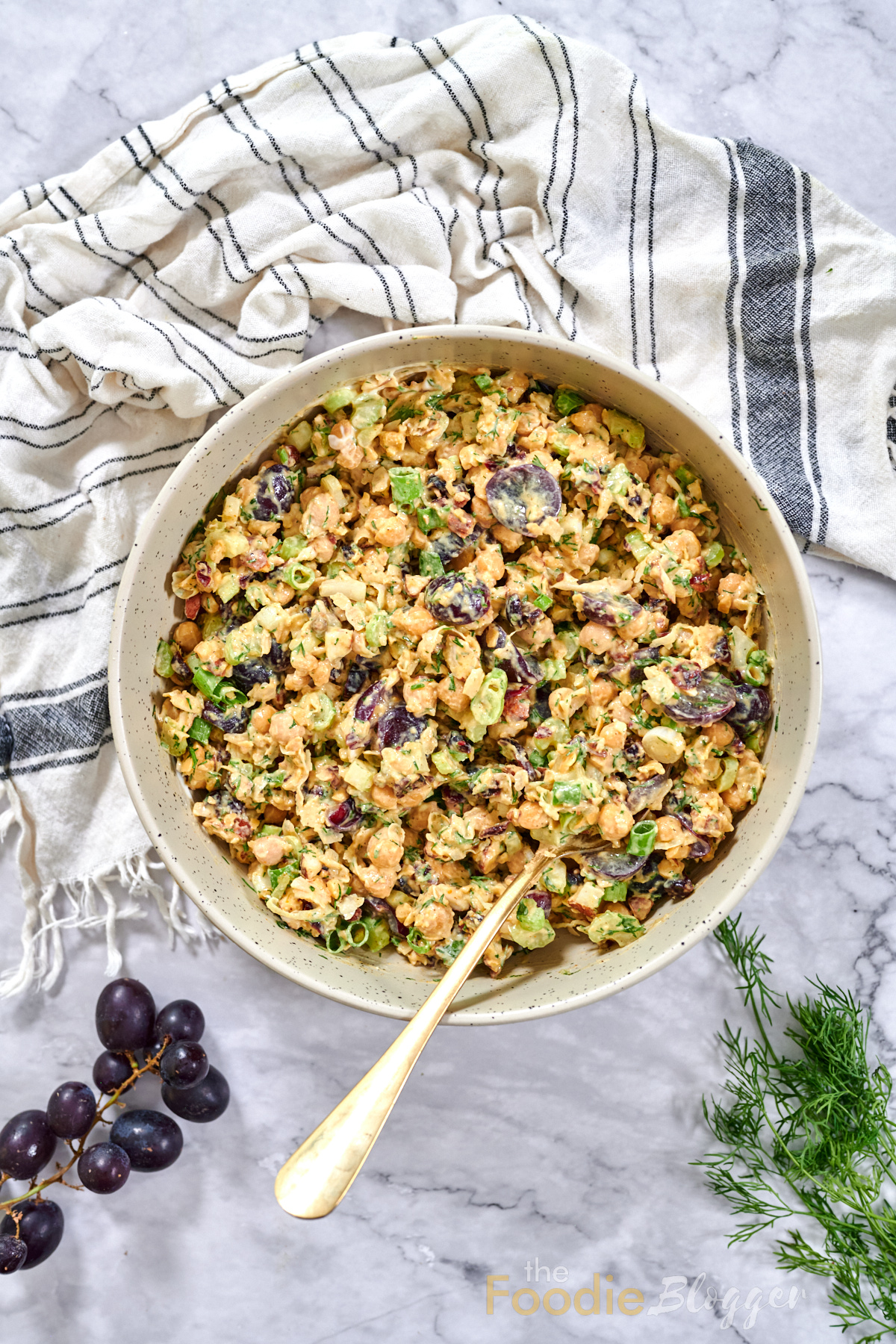 Vegan Chicken Salad 1 Overhead view of a large bowl of chickpea salad dotted with grapes, celery, and green onions, spoon ready for serving.