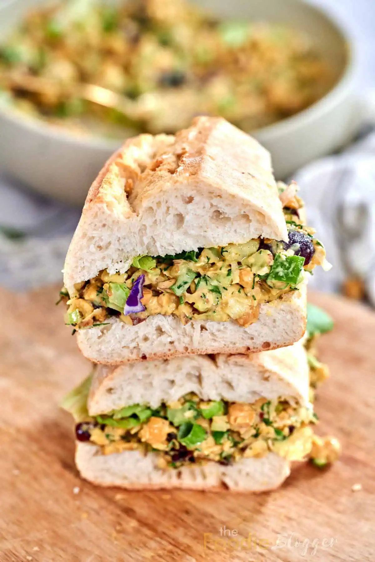 Vegan Chicken Salad 4 Two halves of a vegan chicken-salad sandwich stacked tall on a wooden board.