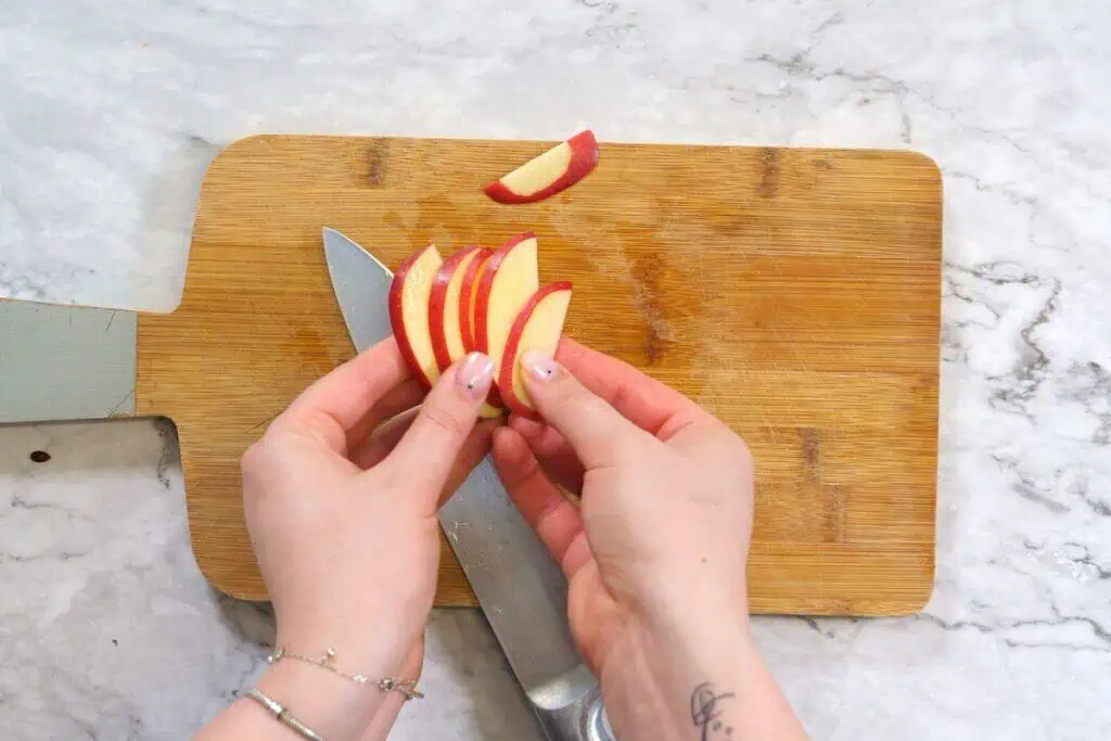 Apple Walnut Salad 5 Fresh red apple slices being prepared on a wooden cutting board.