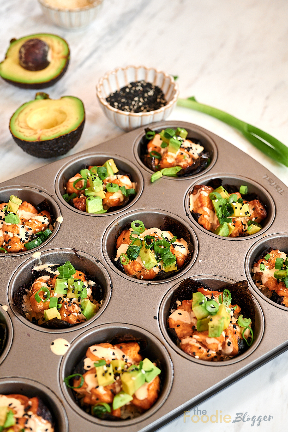 Baked Salmon Sushi Cups 2 Baked salmon sushi cups in a muffin tin topped with avocado and sesame seeds.