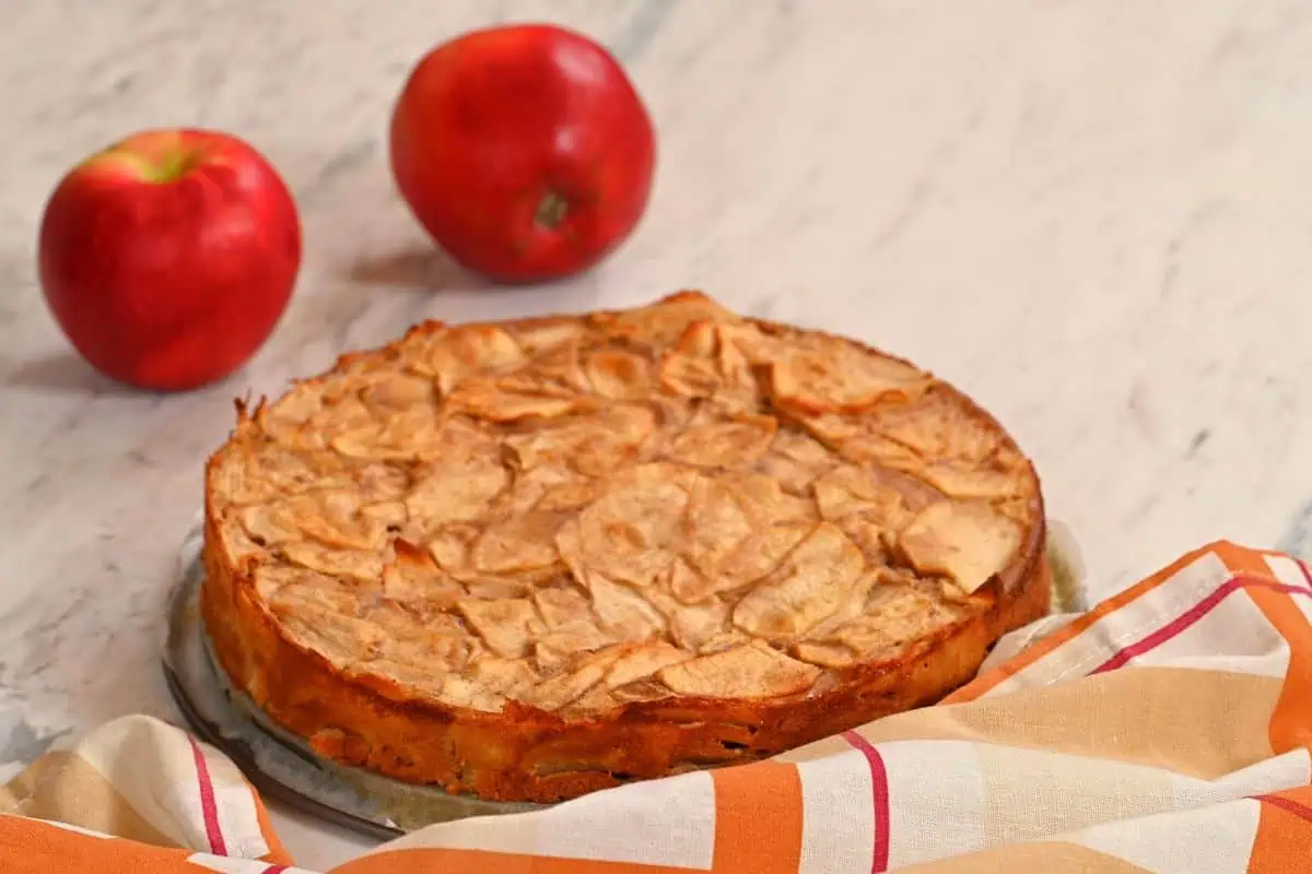 Invisible Apple Cake 11 Whole baked invisible apple cake with golden crust on marble background.