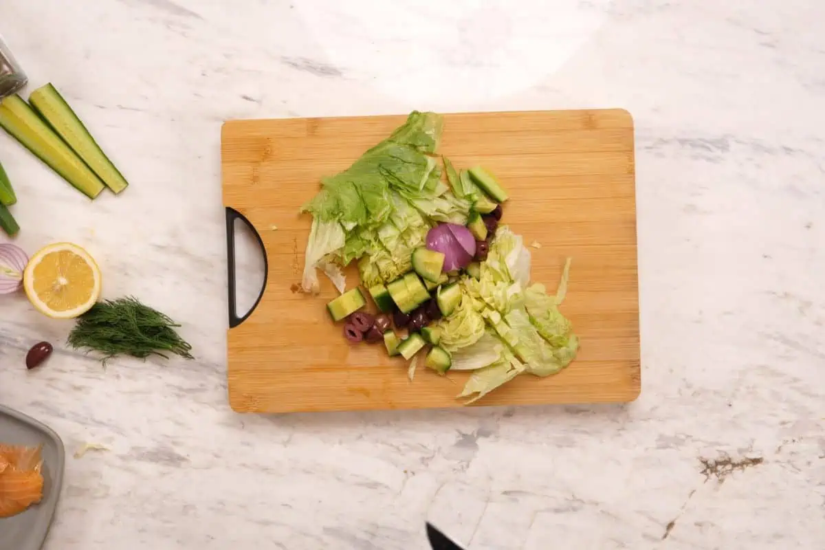 Viral Smoked Salmon Chopped Salad Bagel 4 Chopped iceberg lettuce, smoked salmon, red onion, cucumber, olives, and fresh dill on a cutting board