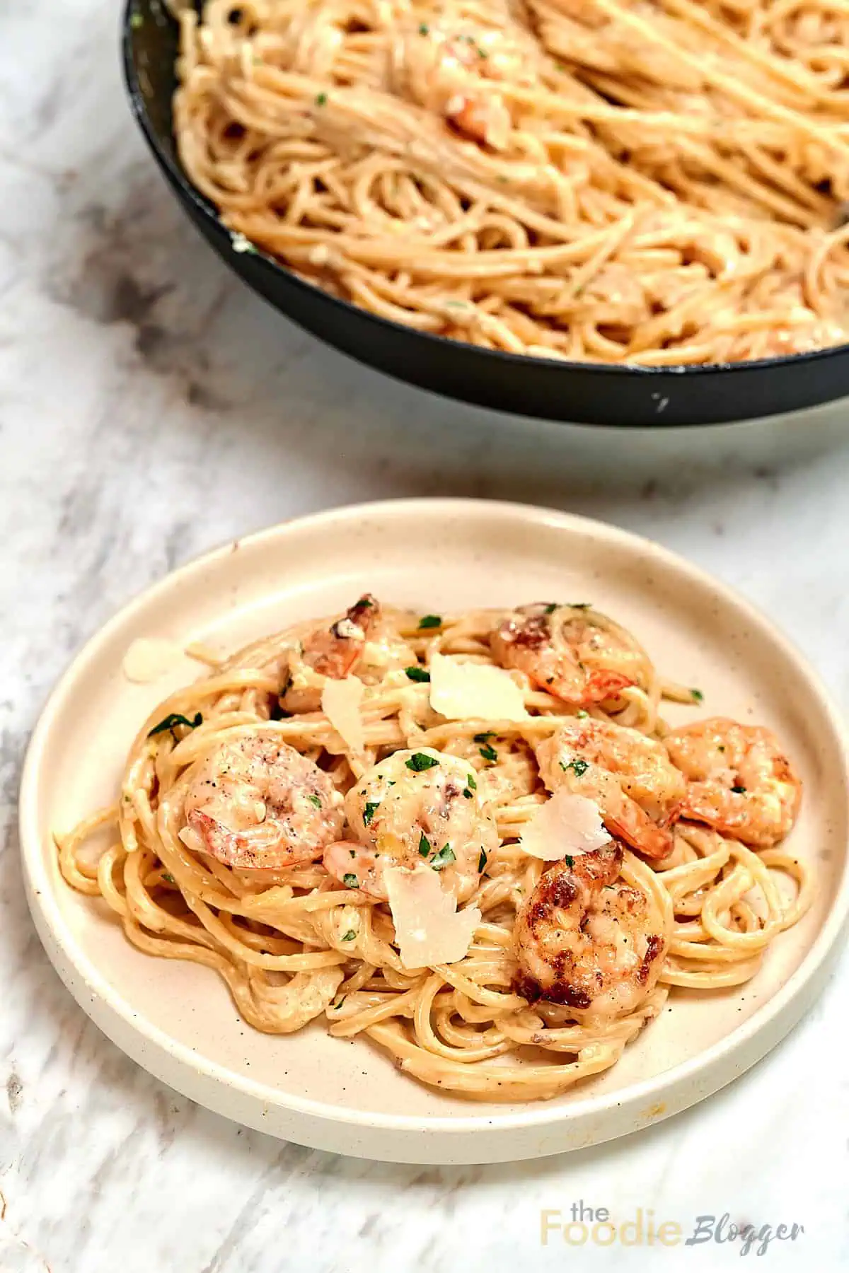 Ultra Creamy Garlic Parmesan Shrimp Pasta 14 Plate of ultra creamy garlic parmesan shrimp pasta with golden seared shrimp and parmesan shavings, skillet of pasta in the background