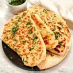 Stack of homemade 2-ingredient garlic butter naan brushed with garlic herb butter on a wooden serving board.