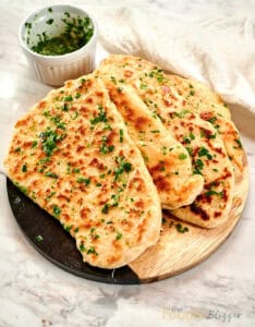 Stack of homemade 2-ingredient garlic butter naan brushed with garlic herb butter on a wooden serving board.
