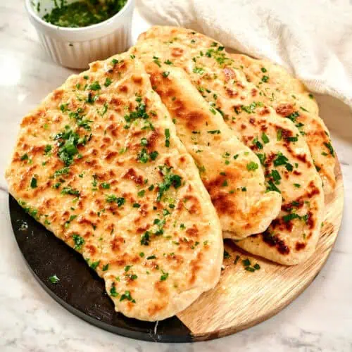 2-Ingredient Garlic Butter Naan 13 Stack of homemade 2-ingredient garlic butter naan brushed with garlic herb butter on a wooden serving board.