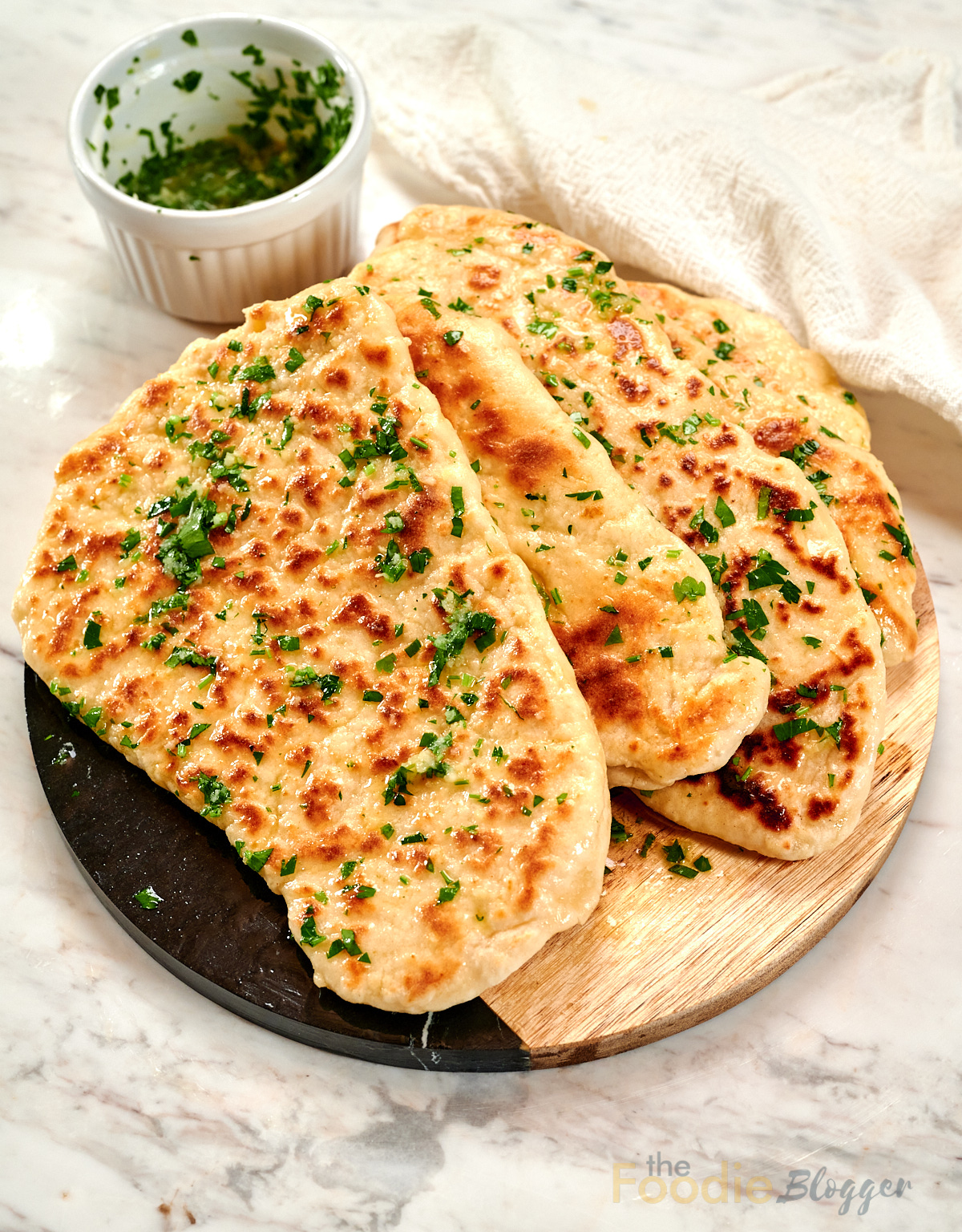 The Foodie Blogger - Tried, True, and Delicious Recipes 3 Stack of homemade 2-ingredient garlic butter naan brushed with garlic herb butter on a wooden serving board.