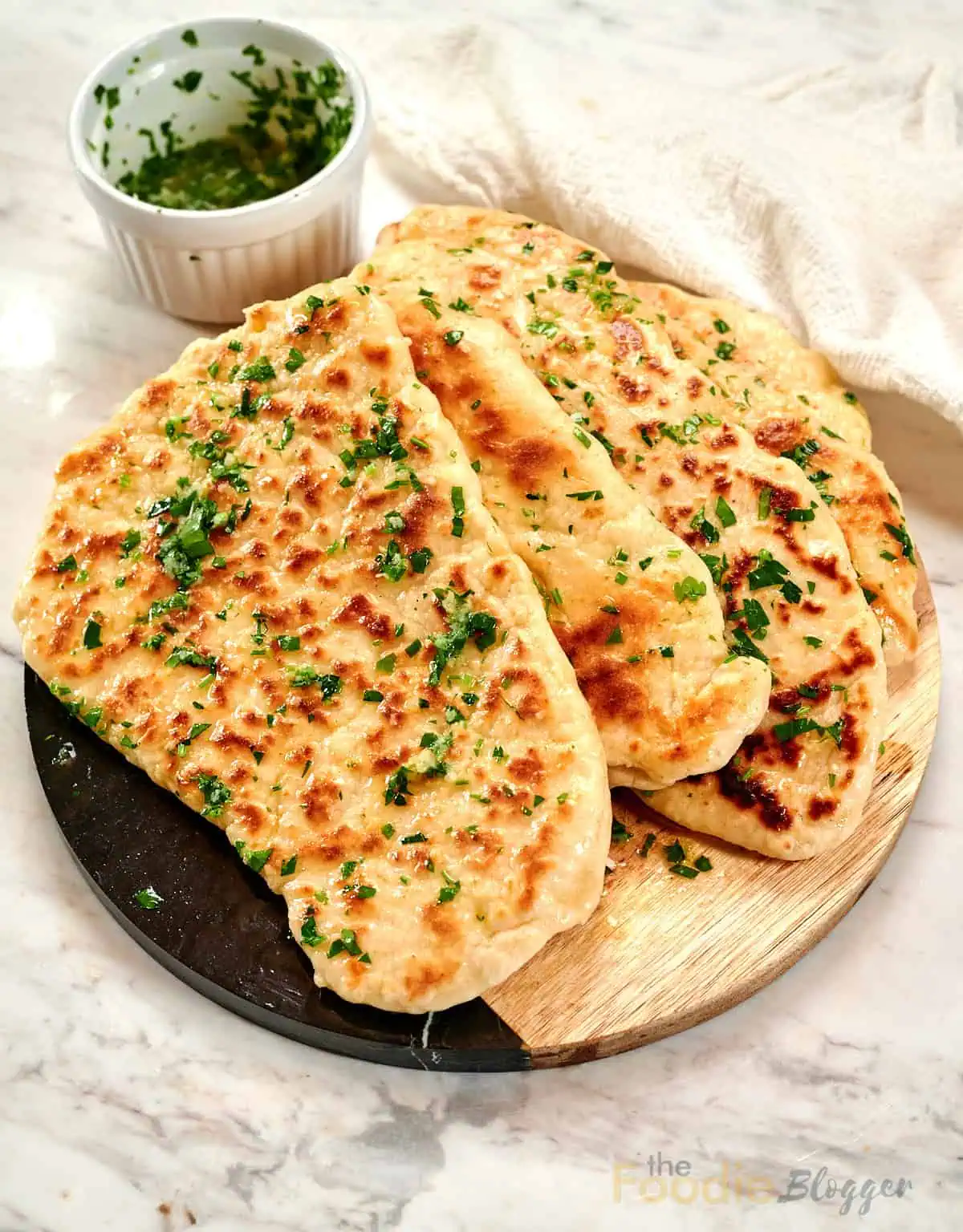 The Foodie Blogger - Tried, True, and Delicious Recipes 1 Stack of homemade 2-ingredient garlic butter naan brushed with garlic herb butter on a wooden serving board.