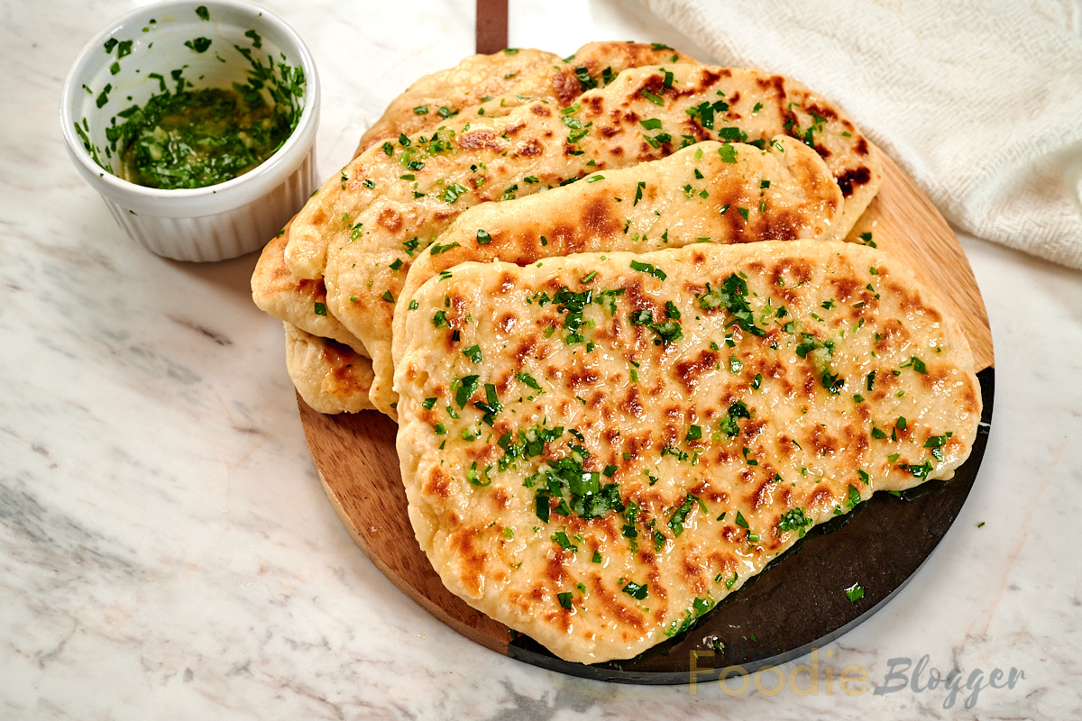 2-Ingredient Garlic Butter Naan 11 Overhead view of fluffy garlic butter naan flatbreads topped with fresh parsley and melted butter.