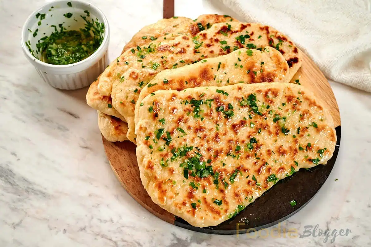 2-Ingredient Garlic Butter Naan 11 Overhead view of fluffy garlic butter naan flatbreads topped with fresh parsley and melted butter.