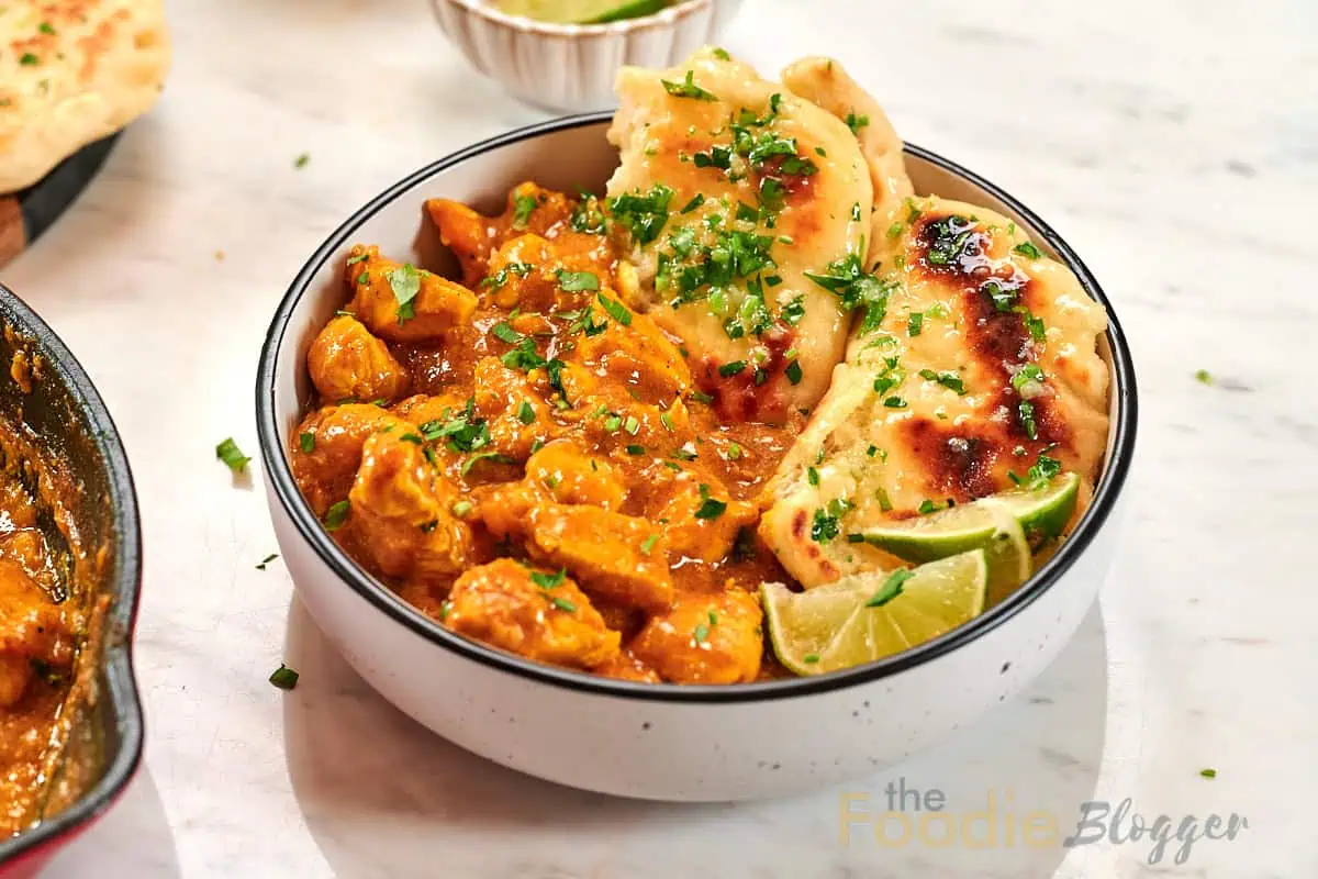 Creamy Chicken Coconut Curry 13 Close-up bowl of creamy chicken coconut curry served with garlic naan and fresh lime wedges.
