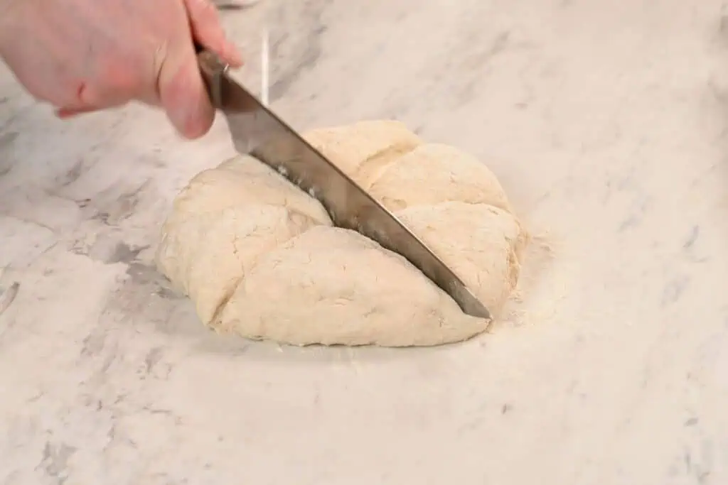 2-Ingredient Garlic Butter Naan 5 Knife cutting the naan dough into equal portions on a lightly floured surface.