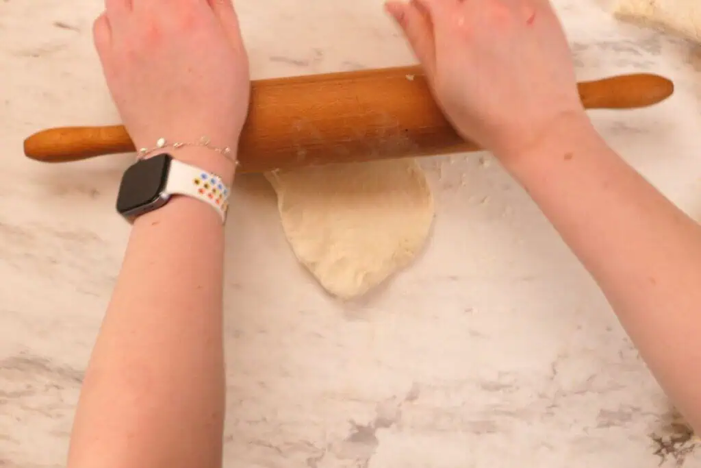 2-Ingredient Garlic Butter Naan 6 Rolling pin flattening a piece of naan dough into an oval shape on the counter.