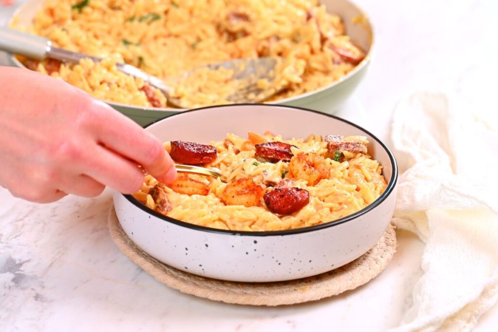 Creamy Cajun Shrimp Orzo 14 Serving creamy Cajun shrimp orzo in a bowl topped with shrimp and sausage slices.